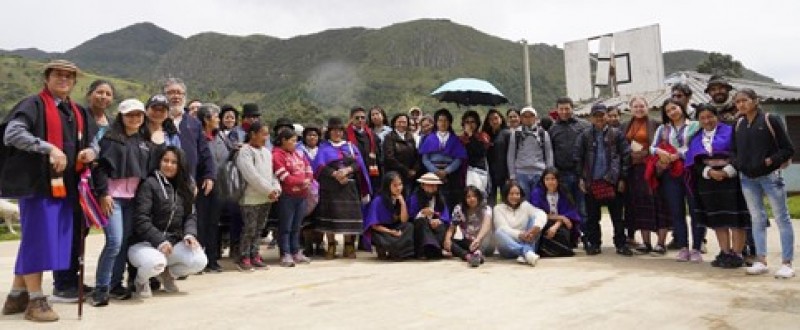 Agroecology course participants stand grouped together for a photo in two rows, with some people kneeling. One person holds up an umbrella, and the green covered mountains are visible behind.